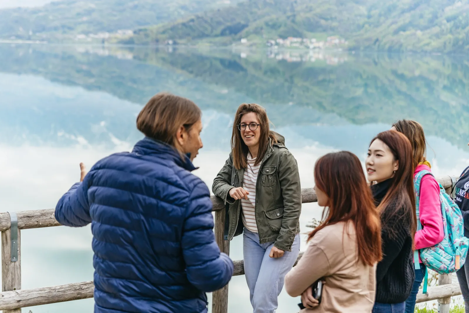 Group of travellers at a wooden railing looking out over a mist-covered alpine lake
