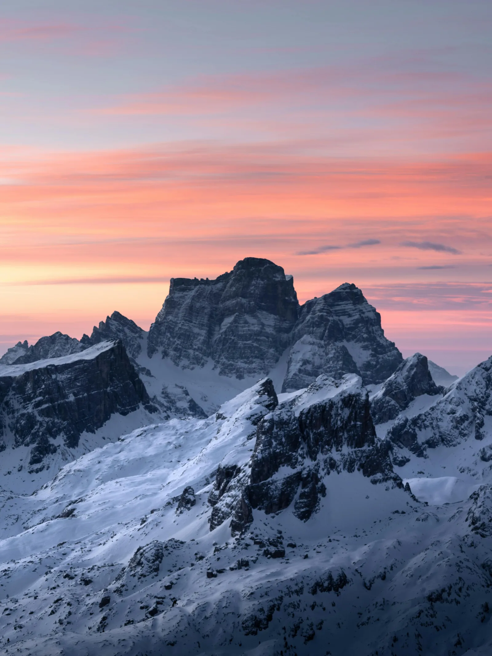Snow-covered Dolomite peaks at dawn under a pink and orange sky