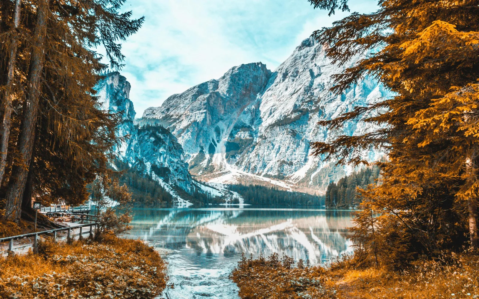 Lake Braies in autumn, turquoise water framed by golden larches with the rock wall of Croda del Becco behind