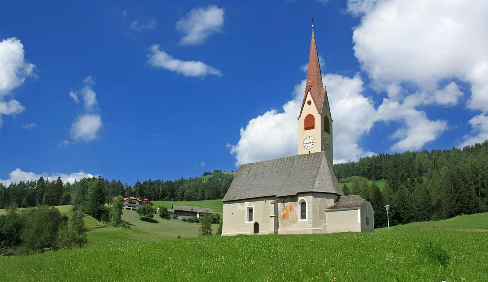 Small white alpine church with a pointed spire on a green meadow in the Pusteria valley
