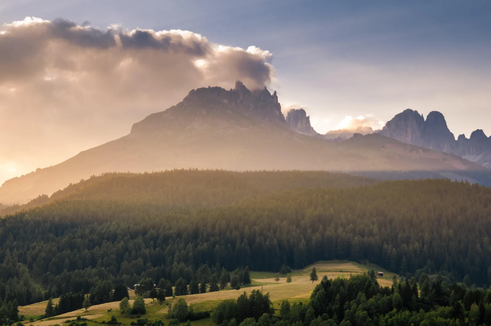 Mist and low cloud over a forested Dolomites valley at sunrise with peaks catching first light