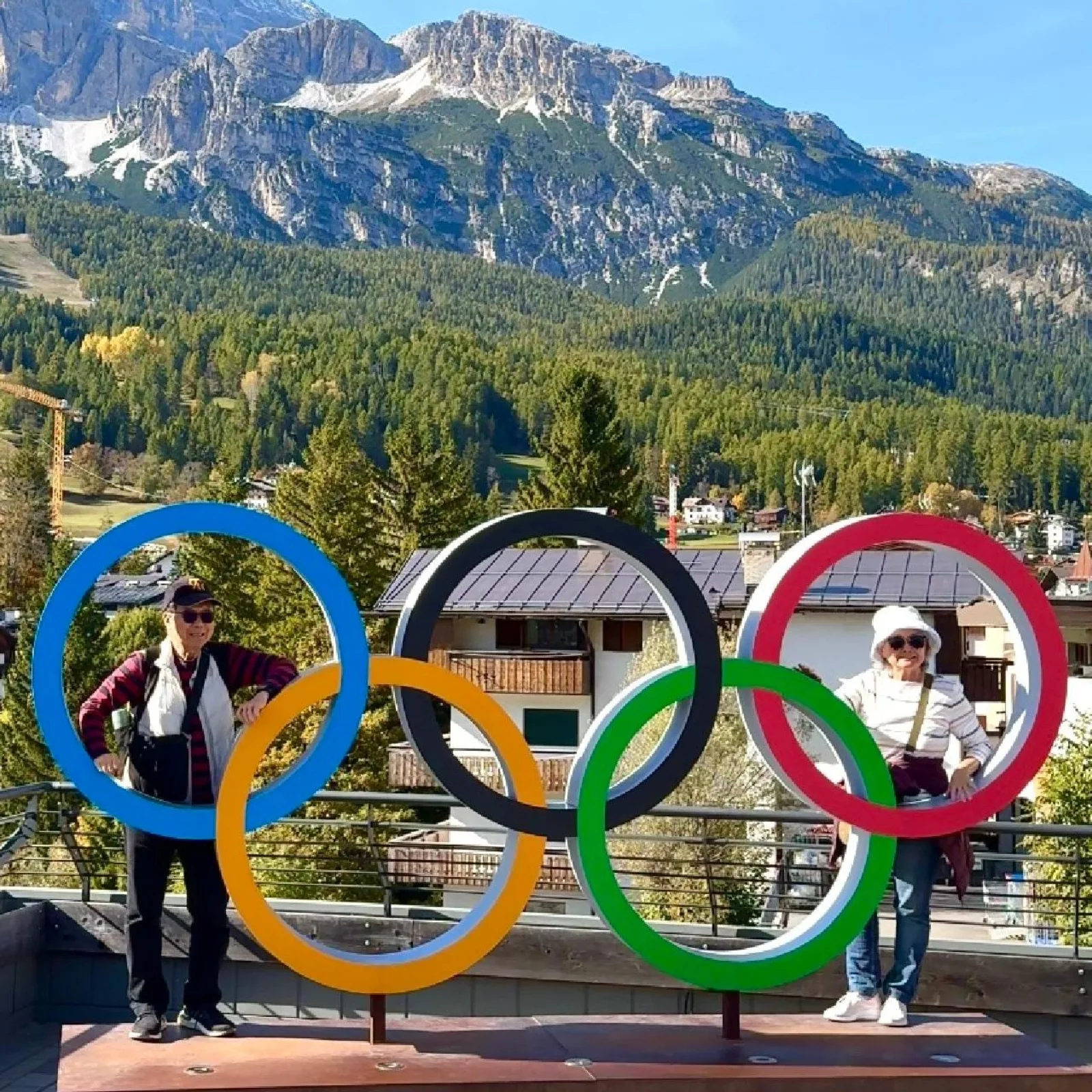 Two travellers standing inside the Olympic rings monument above Cortina d'Ampezzo