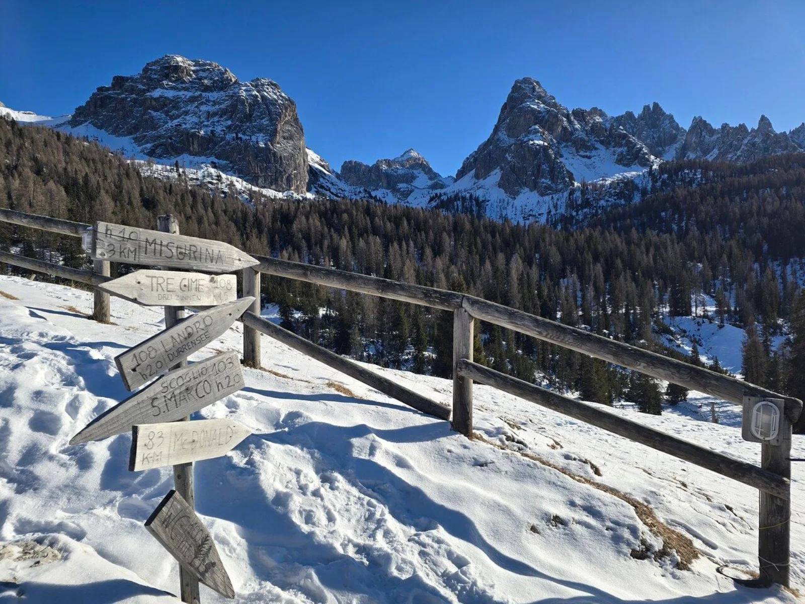 Snow-covered wooden signpost pointing to Misurina and the Tre Cime with peaks behind