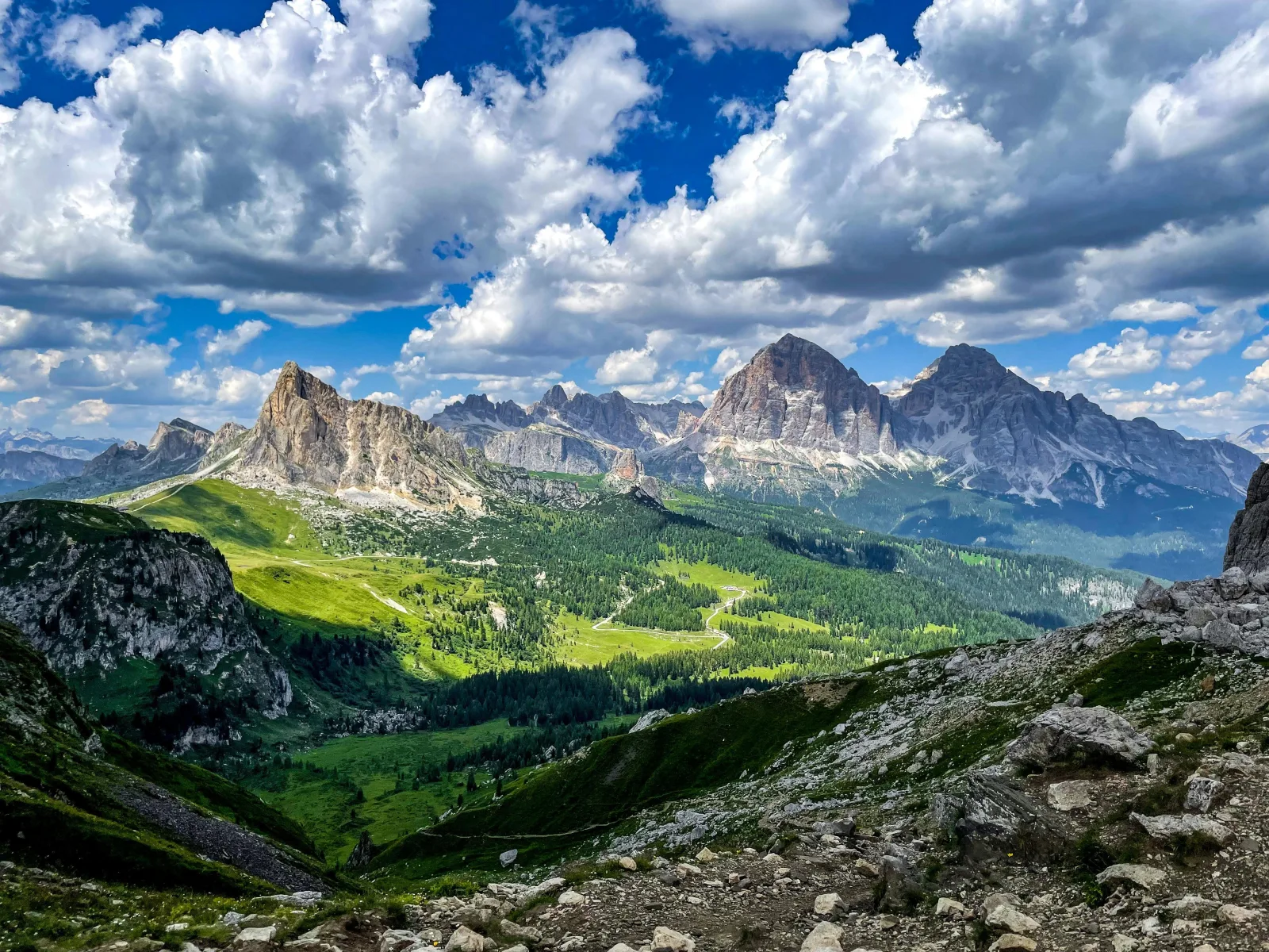 Panorama of green Dolomite valleys and rock towers seen from a high pass on the Cortina route