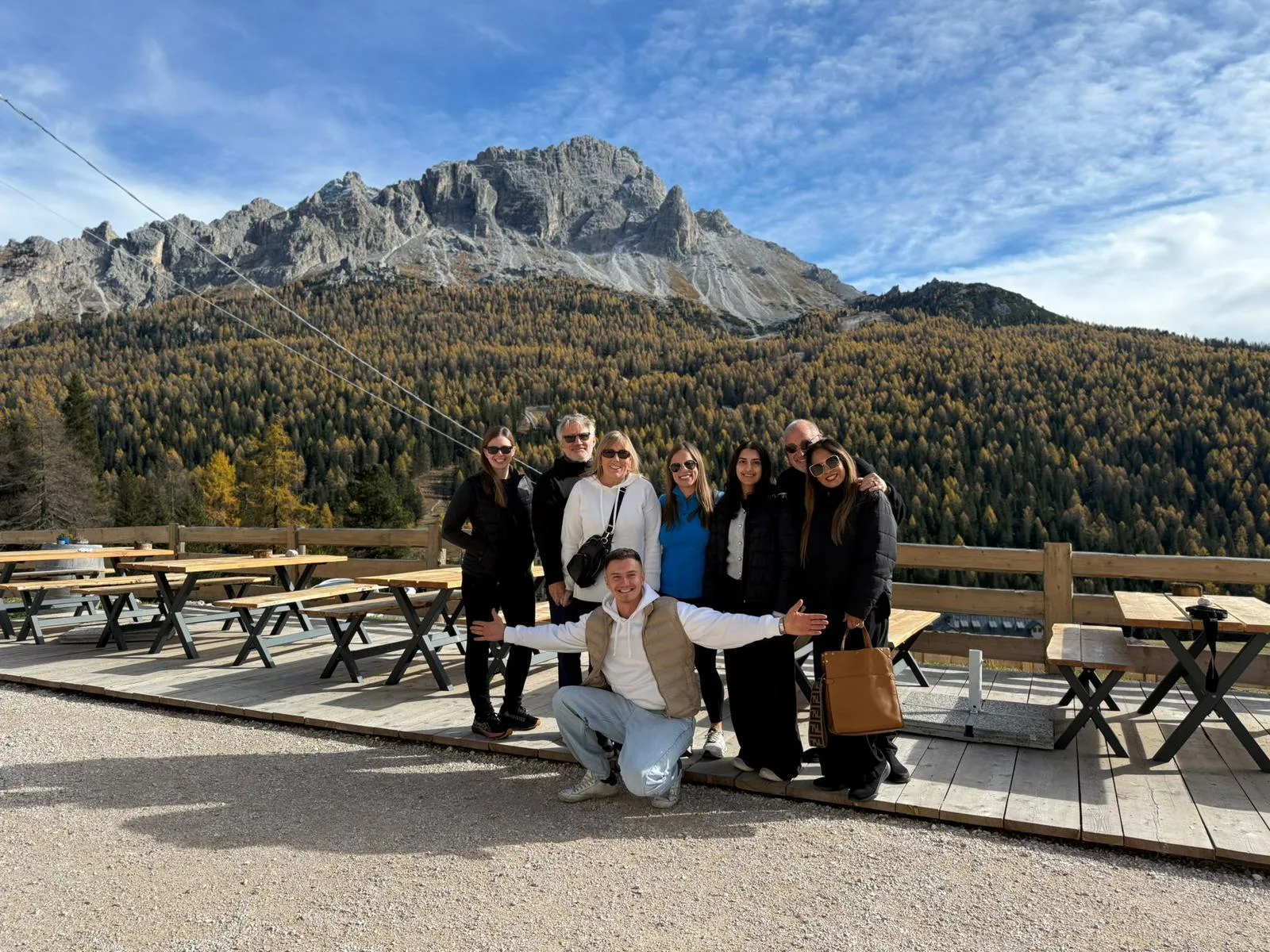 Tour group posing on a mountain terrace above Cortina with golden autumn larches on the slopes behind