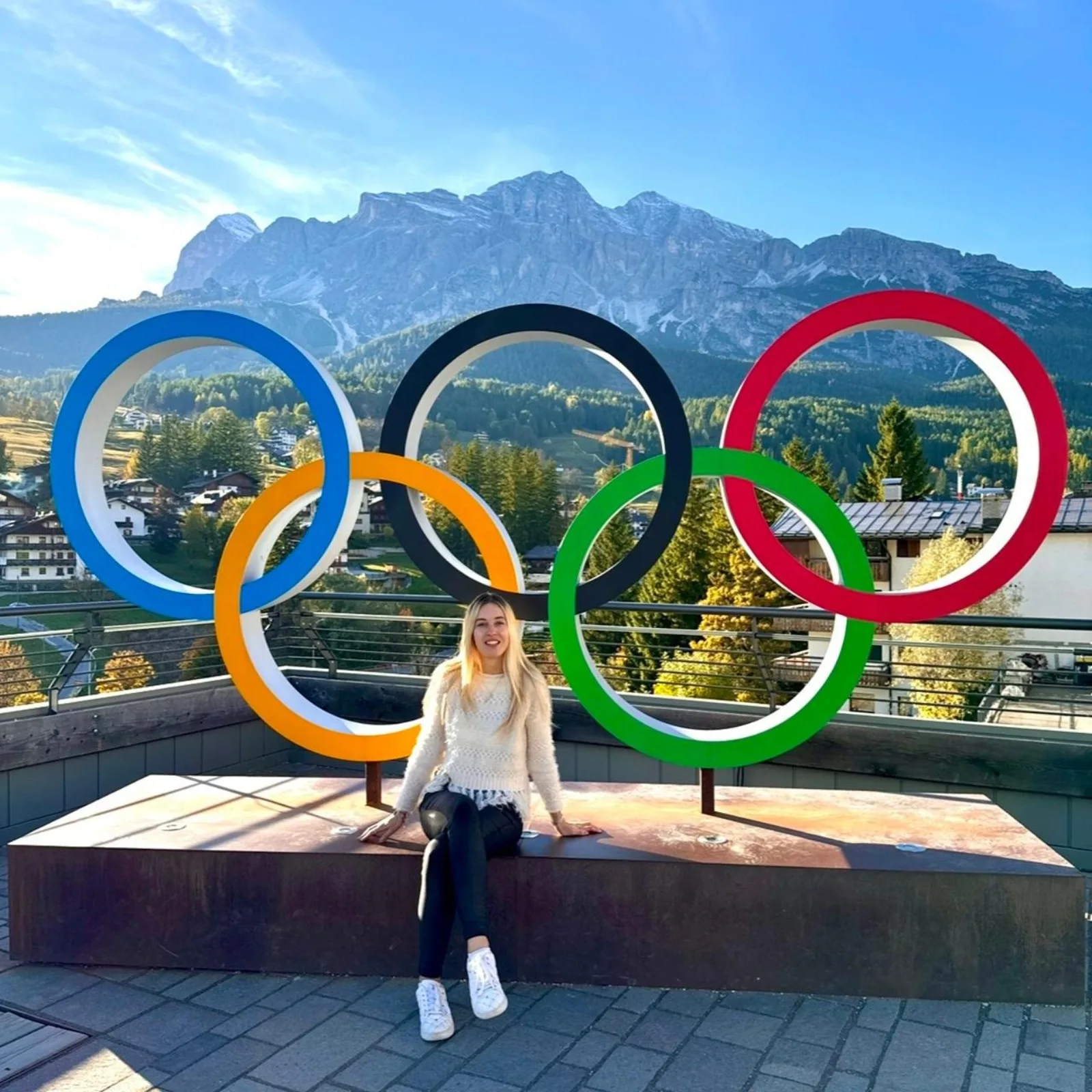 Traveller sitting inside the Olympic rings monument in Cortina d'Ampezzo with Dolomite peaks behind