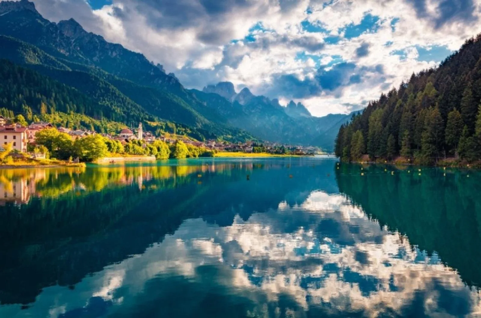 Turquoise alpine lake reflecting cloud with a lakeside village and autumn trees on the bank