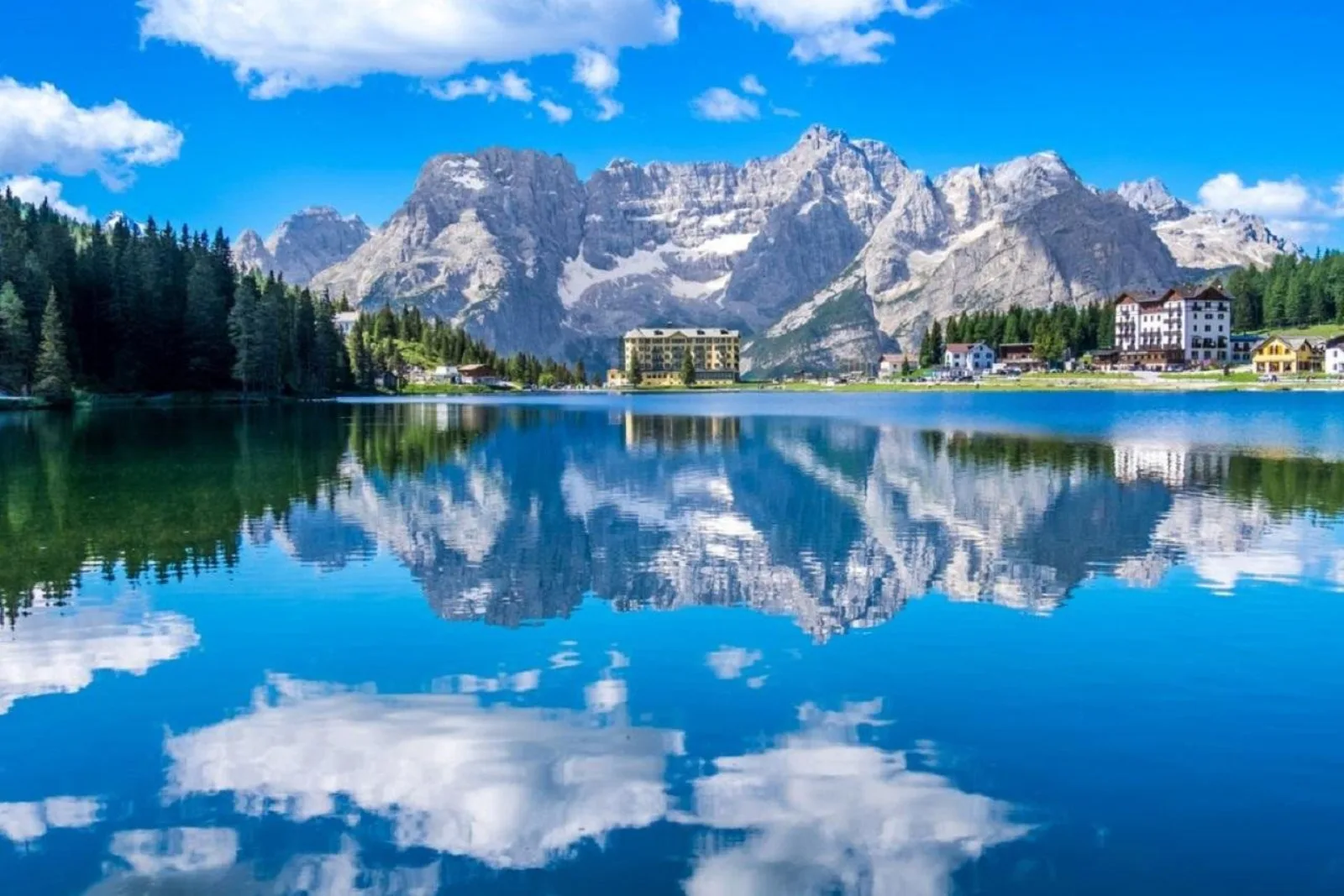 Lake Misurina mirror-still under a blue sky with the Grand Hotel and the Sorapiss group behind