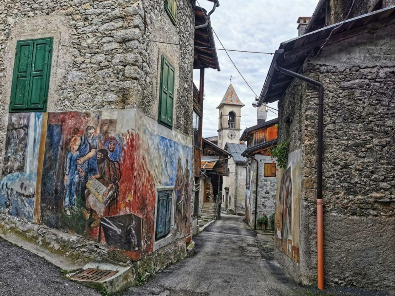 Narrow street in Cibiana di Cadore with a large painted mural on a stone house and the church tower behind