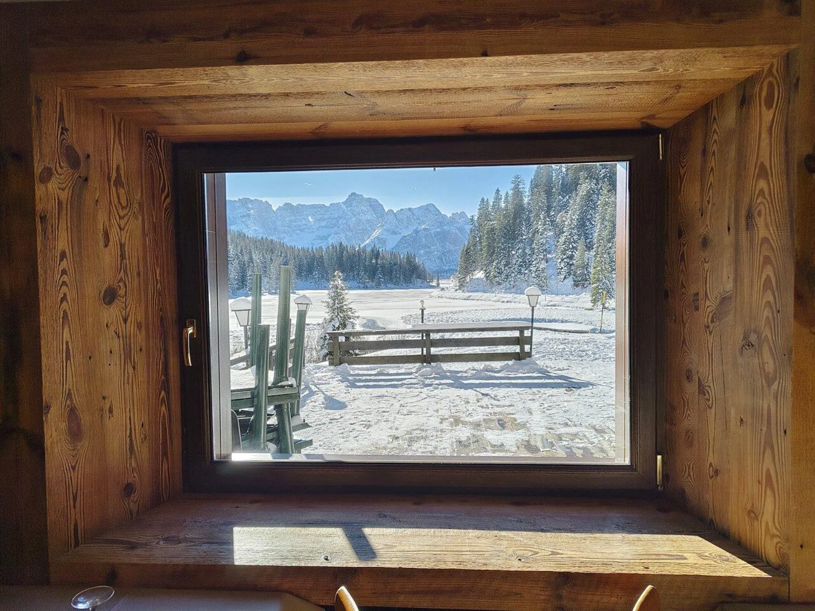 View through the window of a wooden mountain hut onto a snow-covered Dolomites meadow